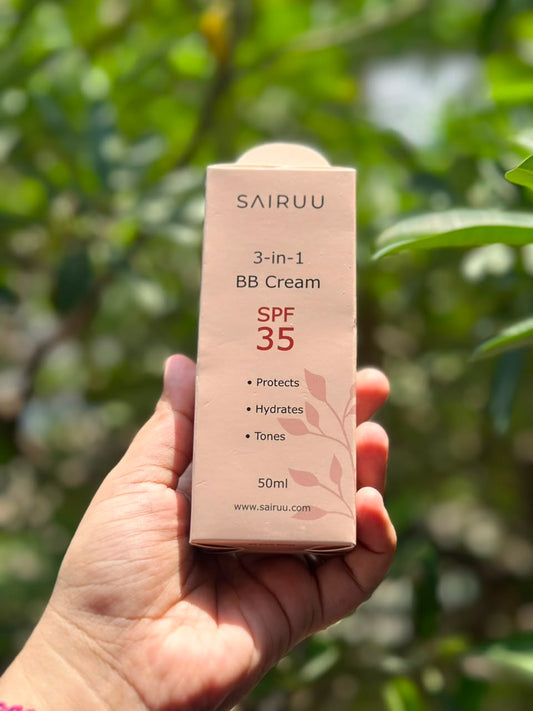 A hand holding a pink box of Sairuu 3-in-1 BB Cream SPF 35, with a blurred green outdoor background.